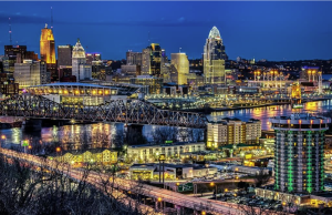 Nighttime cityscape of a riverfront with illuminated bridges and high-rise skyline above the water.